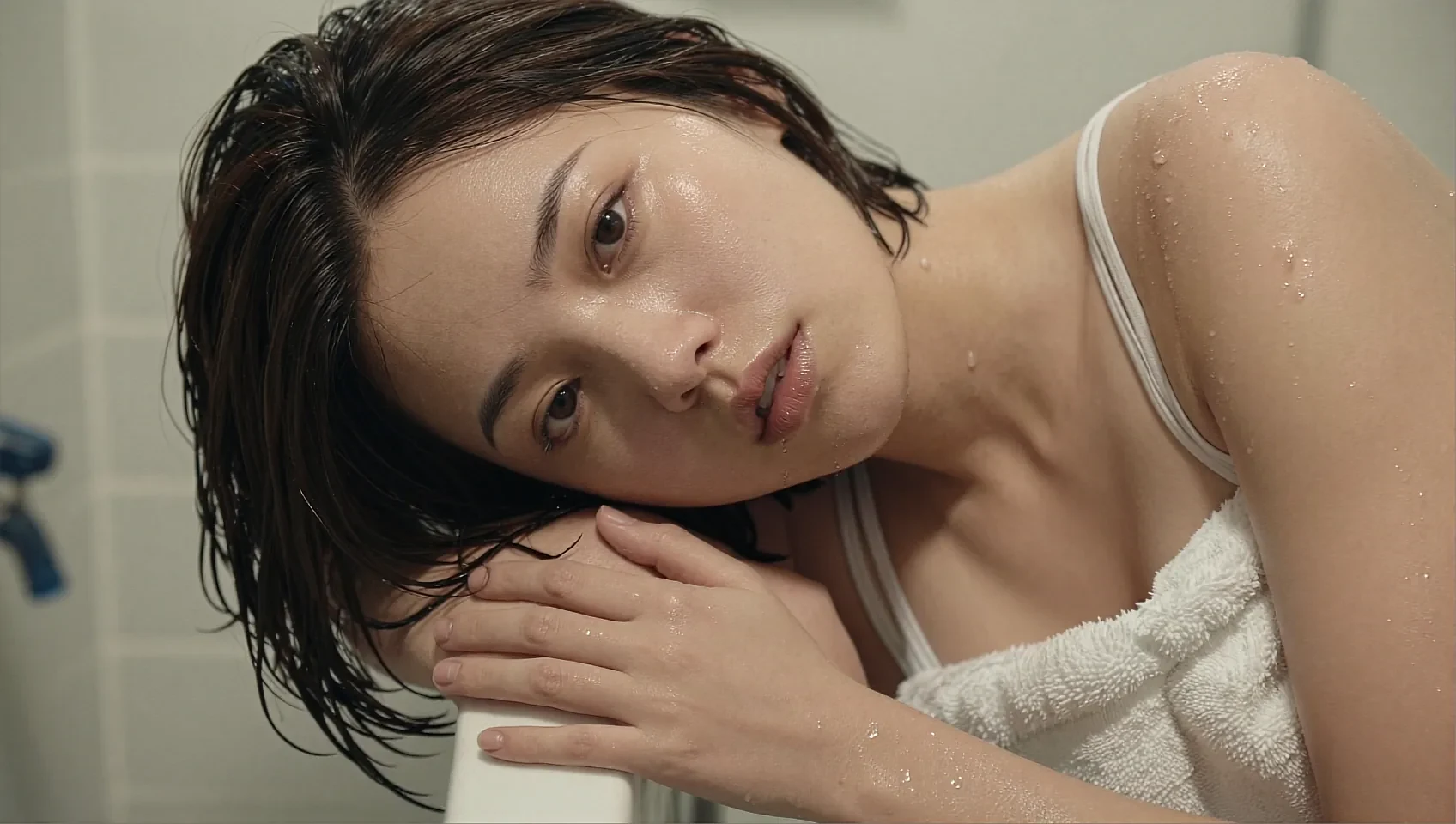 Fictional AI character resting her head on her arms in soft bathroom light, wrapped in a towel
